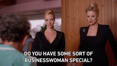 Screenshot from Romy and Michele's High School Reunion, where they're dressed in their black suits and it says "Do you have some sort of businesswoman special?"