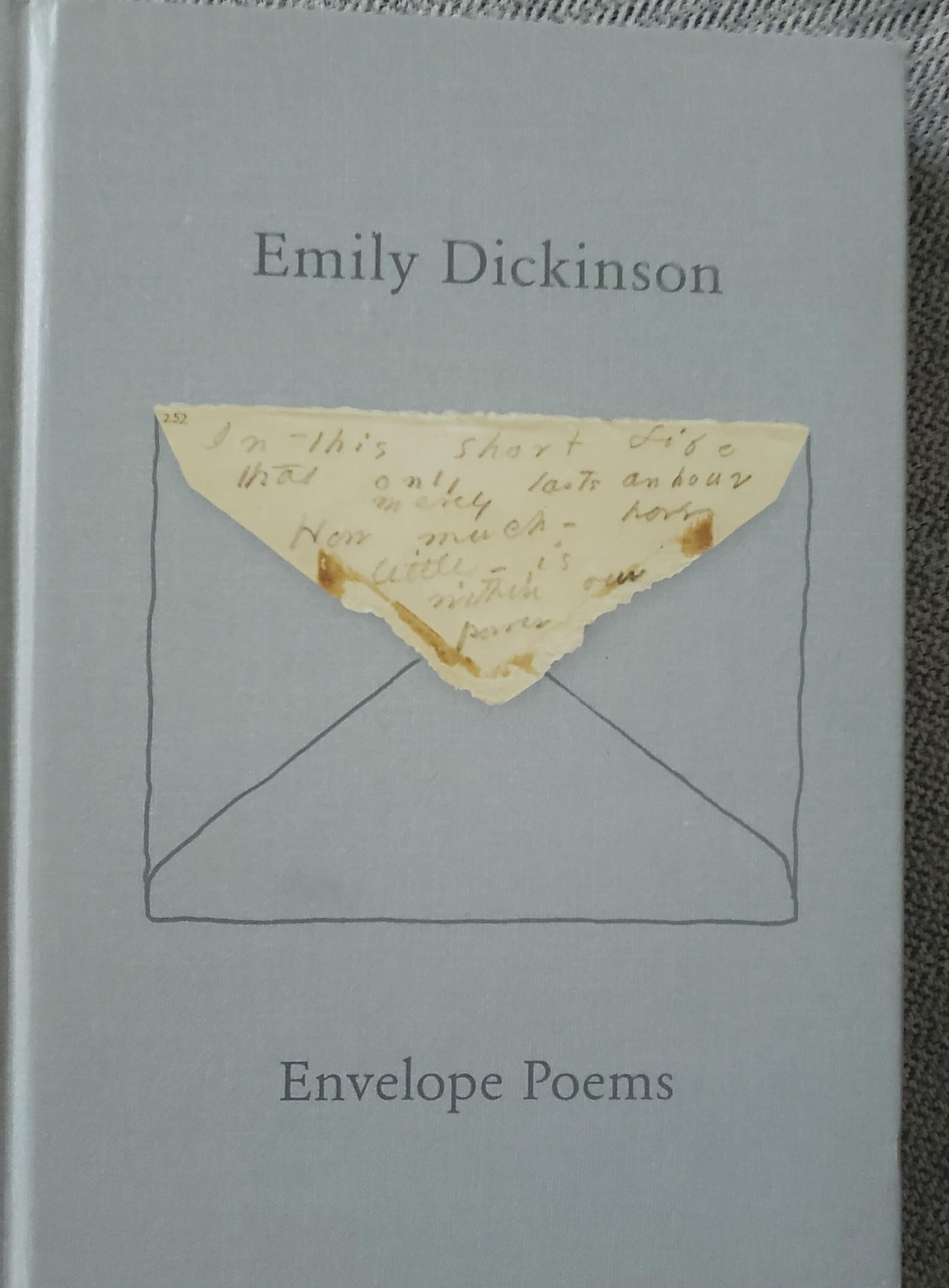 The Envelope Poems book--gray hard cover with the drawing of an envelope in thin black lines. The flap is an image of Dickinson's writing on an envelope flap: In this short life that only lasts an hour how much how little is within our power.