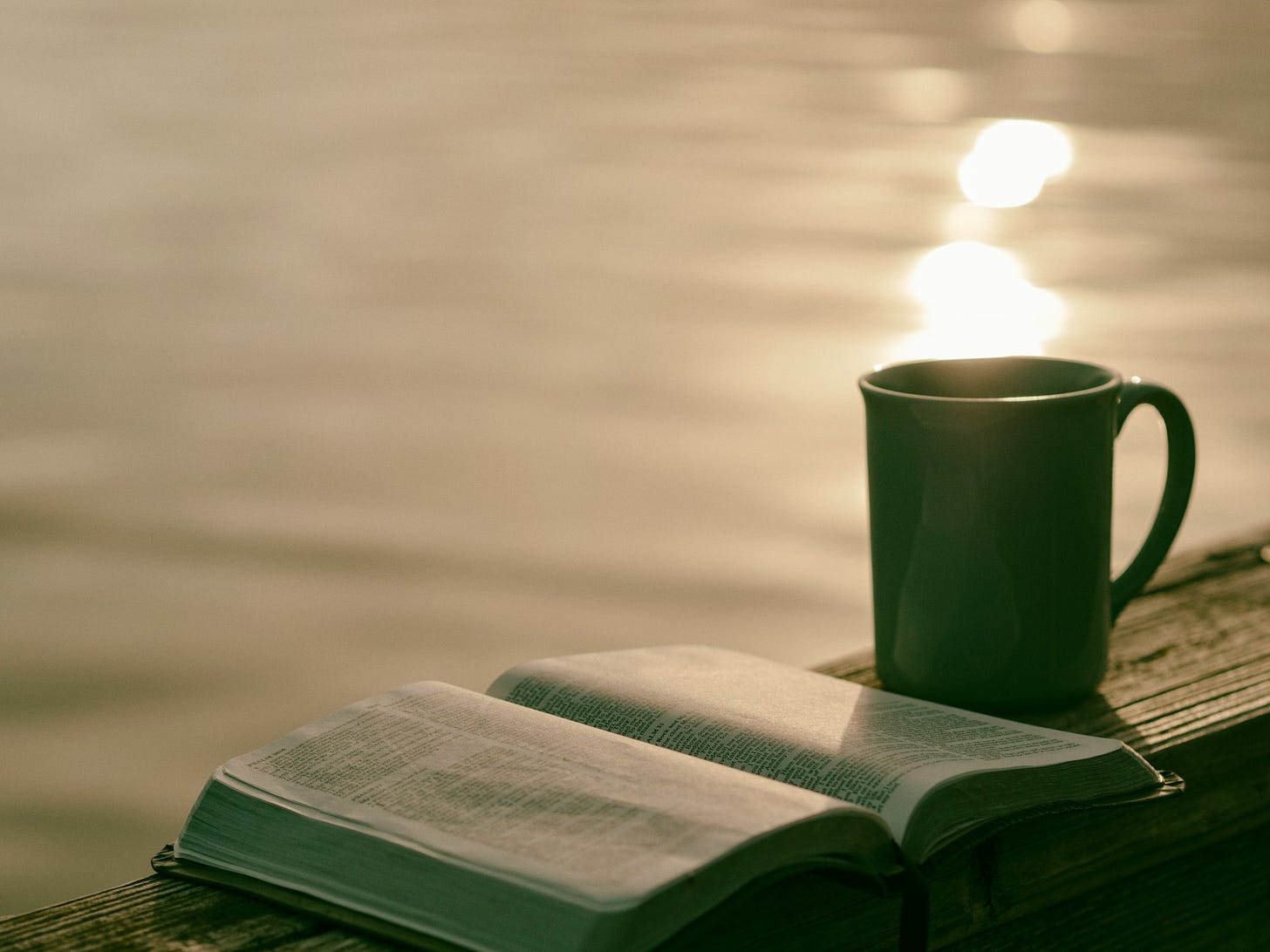 Image of a Bible and coffee mug on railing over a body of water.