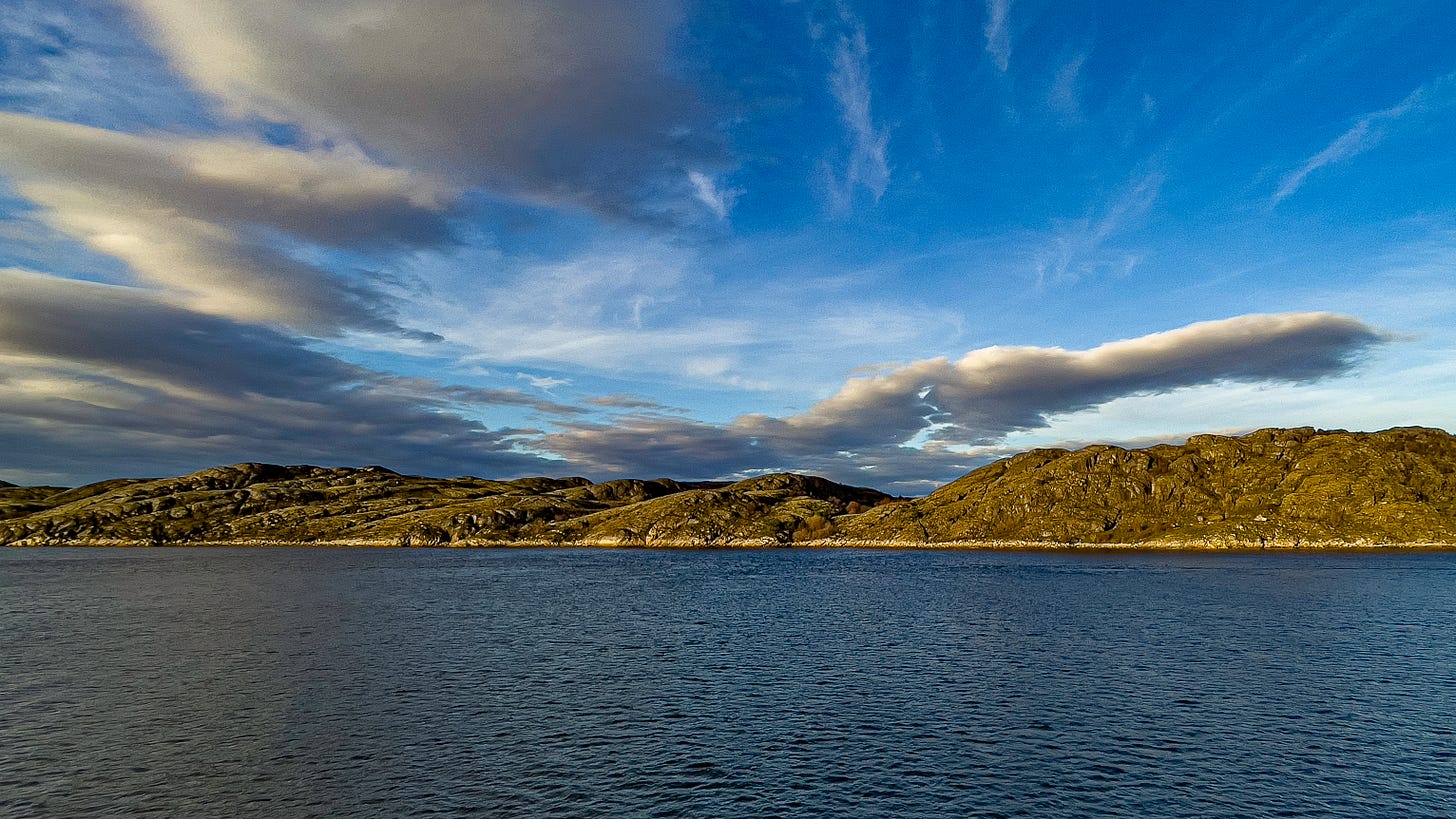 Norwegian coastal landscape with rocky hills illuminated by golden sunlight under a blue sky with scattered clouds, photographed by Jay Siegmann. Norwegian coastal landscape with rocky hills illuminated by golden sunlight under a blue sky with scattered clouds, photographed by Jay Siegmann.