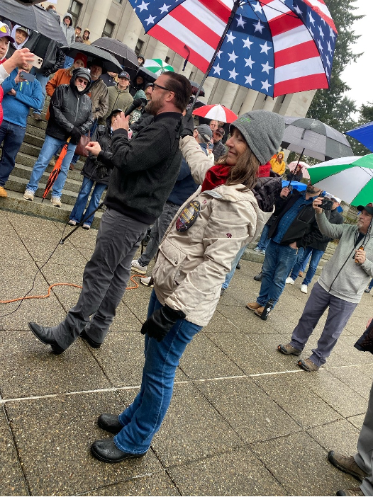 Katie holds the umbrella over speaker Brian Noble from the Family Policy Institute of Washington.