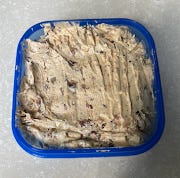 A small blue tuppaware tub, with a buttery looking substance with brown flecks stored in it.