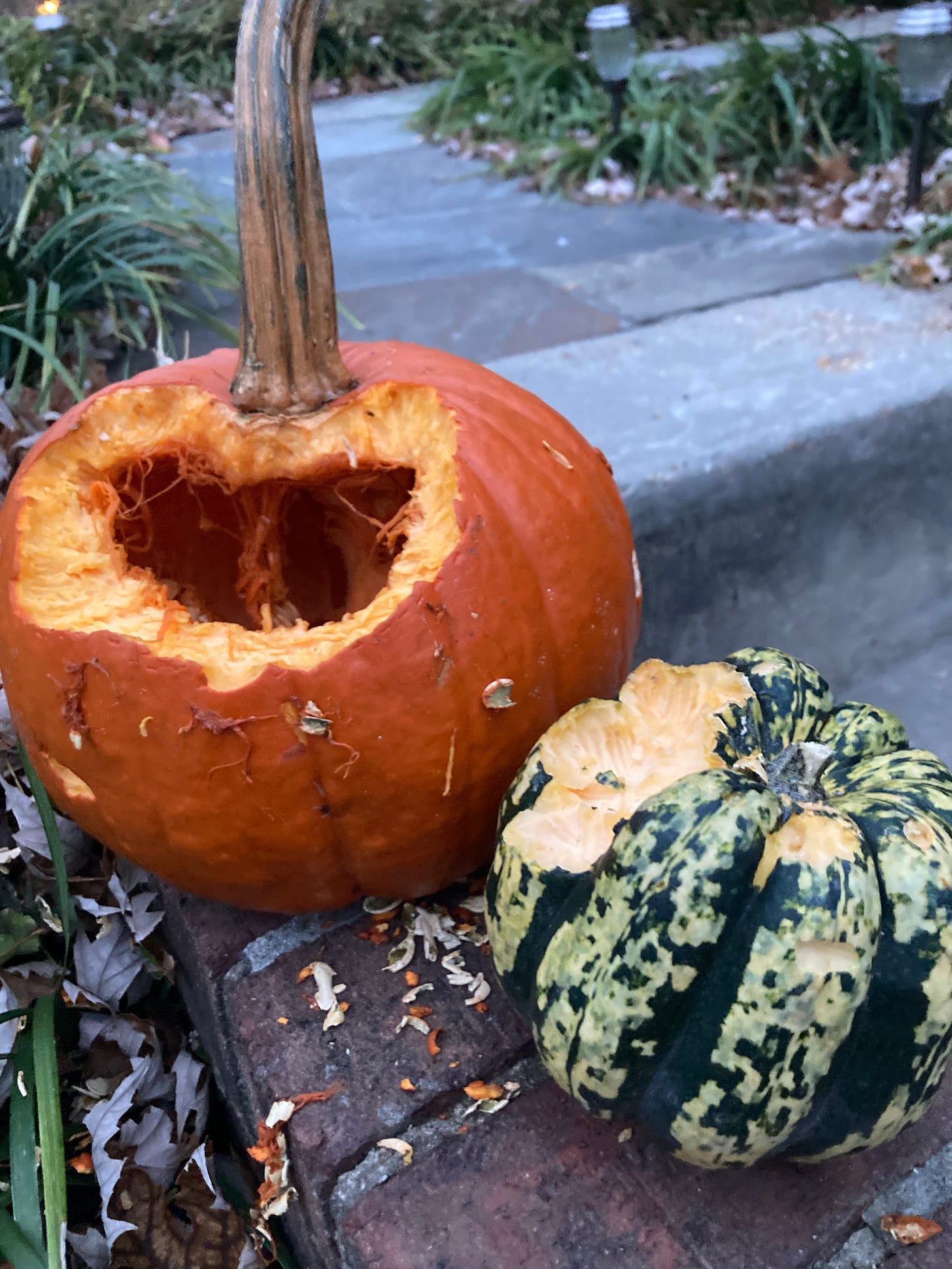 A large orange pumpkin with a large hole on a stoop. A green squash sits in the foreground with tooth marks. 