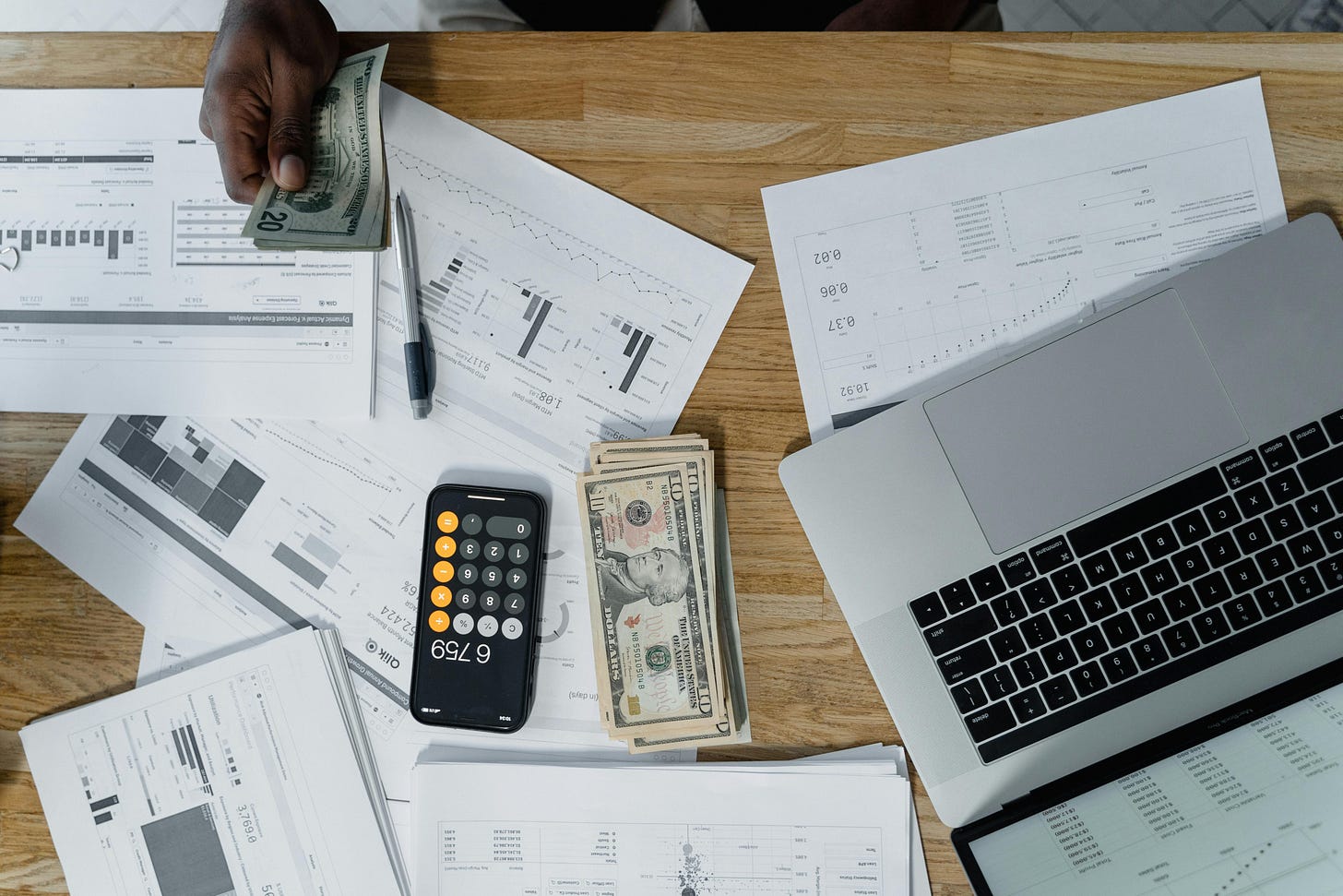 Looking down on a desk full of paperwork, a calculator, a laptop, some cash, and a pen. Looking down on a desk full of paperwork, a calculator, a laptop, some cash, and a pen.