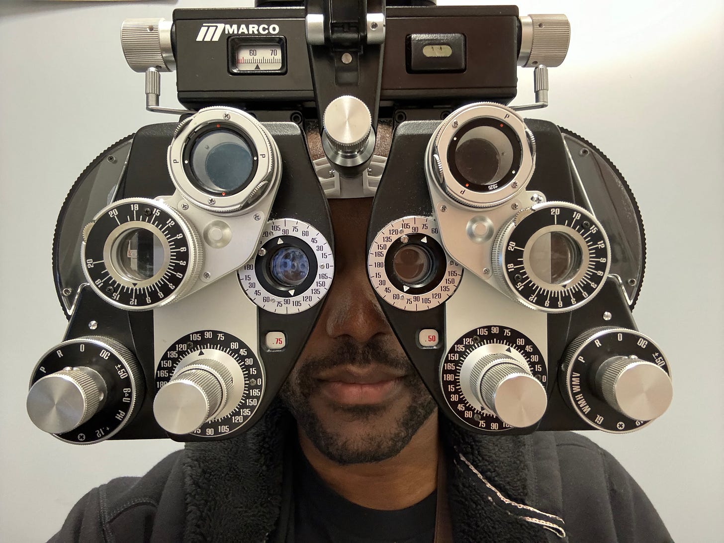 ArmaniXR in his IRL avatar behind a phoropter, which is an eye examination device consisting of different lenses and dials.