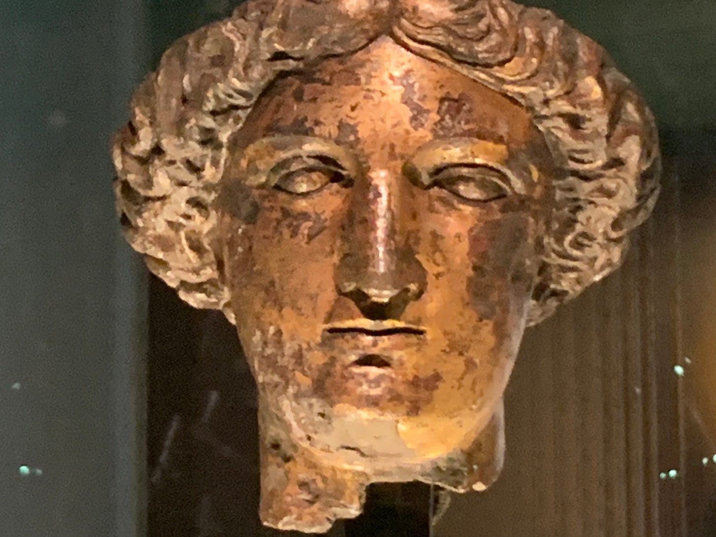 The head of a statue of the goddess Minerva, covered in flaking gold leaf. She has quite the impassive stare.