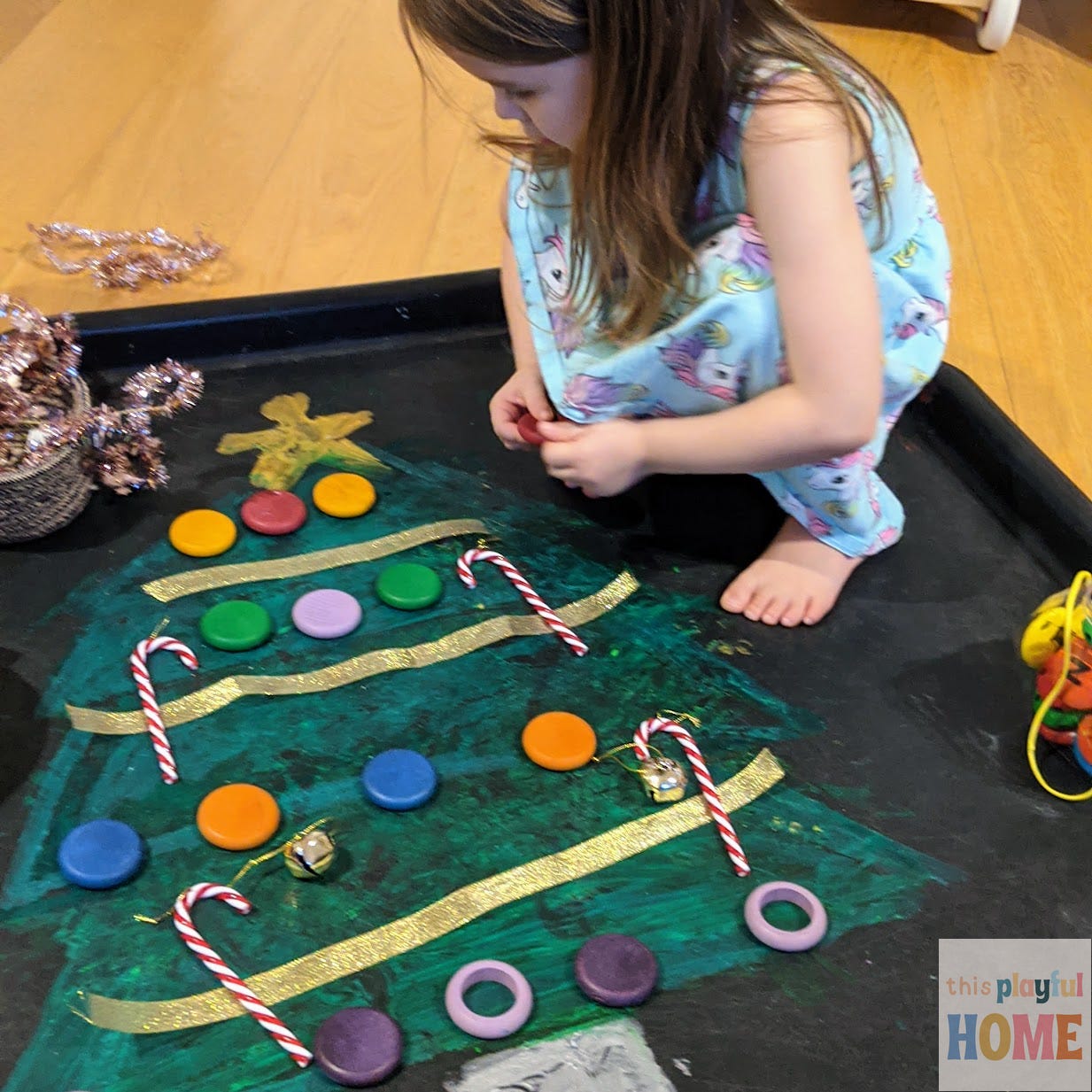 a brown-haired 4 year old girl places loose parts onto a painting a christmas tree