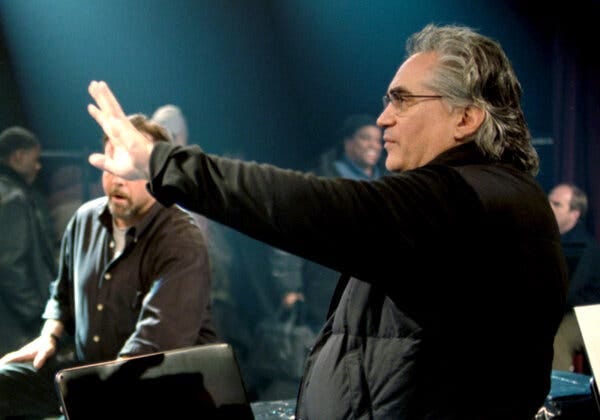 Paul Justman standing with several people behind him. He is wearing a black jacket and glasses and gesturing with his left hand.