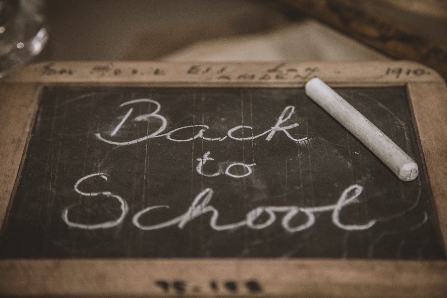 A chalkboard and chalk stick spell out 'back to school' in cursive while lying down, flat 