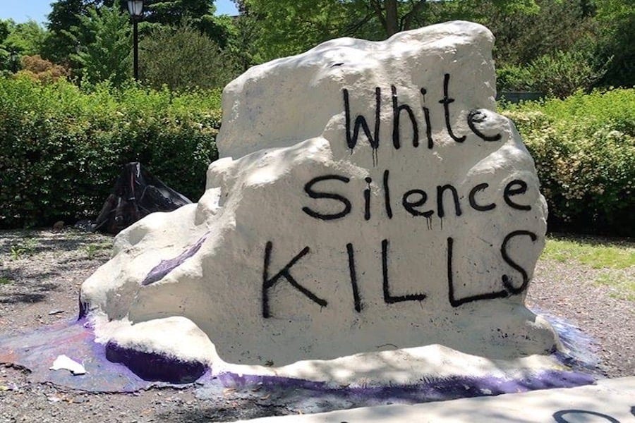 The same rock pictured above is painted all white. “White Silence KILLS” is spray-painted in black ink. Photograph taken on a sunny day in Evanston, Illinois.