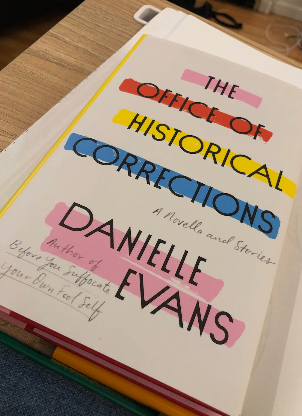 A photo of Kat’s copy of The Office of Historical Corrections by Danielle Evans. The cover is abstract with warm-colored horizontal lines dashing across it.