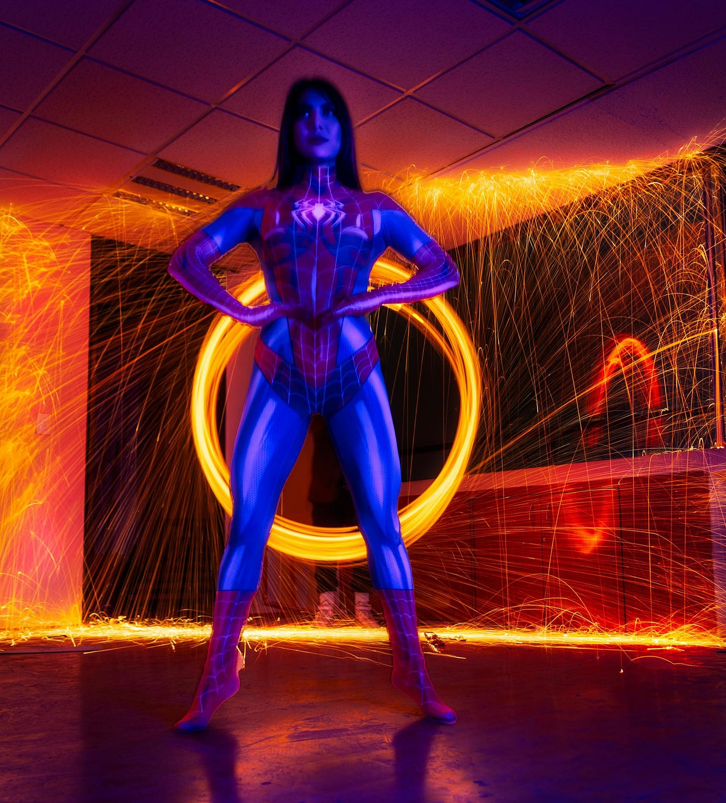 female spiderwoman, standing with hands on hips in a blue suit in a room with welding lights in 