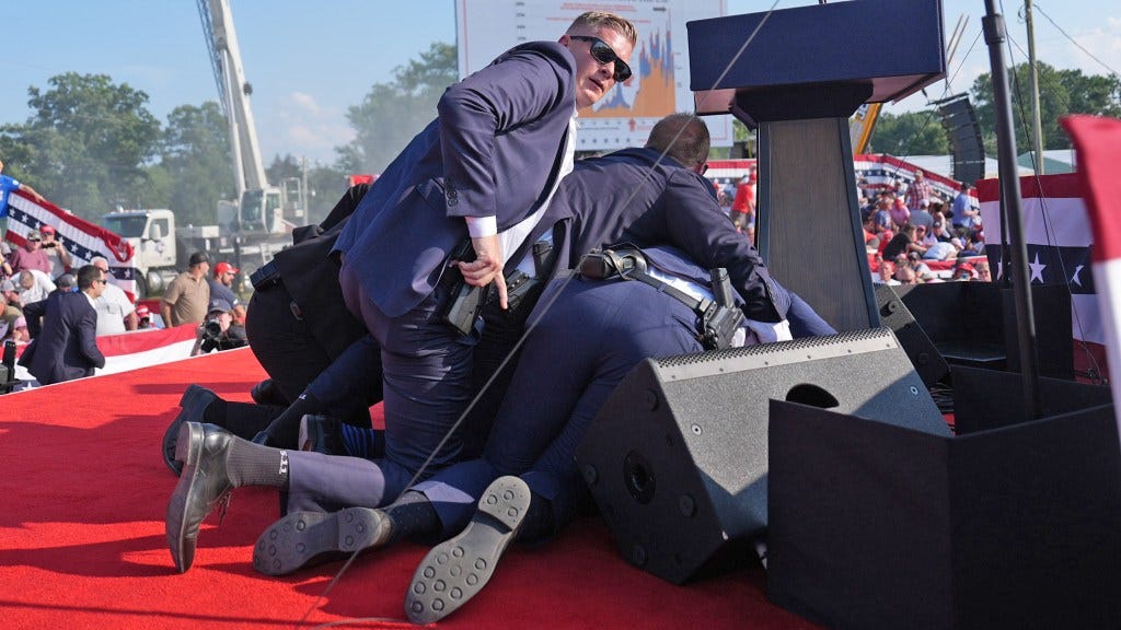 BUTLER, PENNSYLVANIA - July 13: Secret service agents cover former president Donald Trump during a campaign rally for former President Donald Trump at Butler Farm Show Inc. on Saturday, July 13, 2024 in Butler, Pa. Trump ducked and was taken offstage after loud noises were heard after he began speaking. (Photo by Jabin Botsford/The Washington Post via Getty Images)