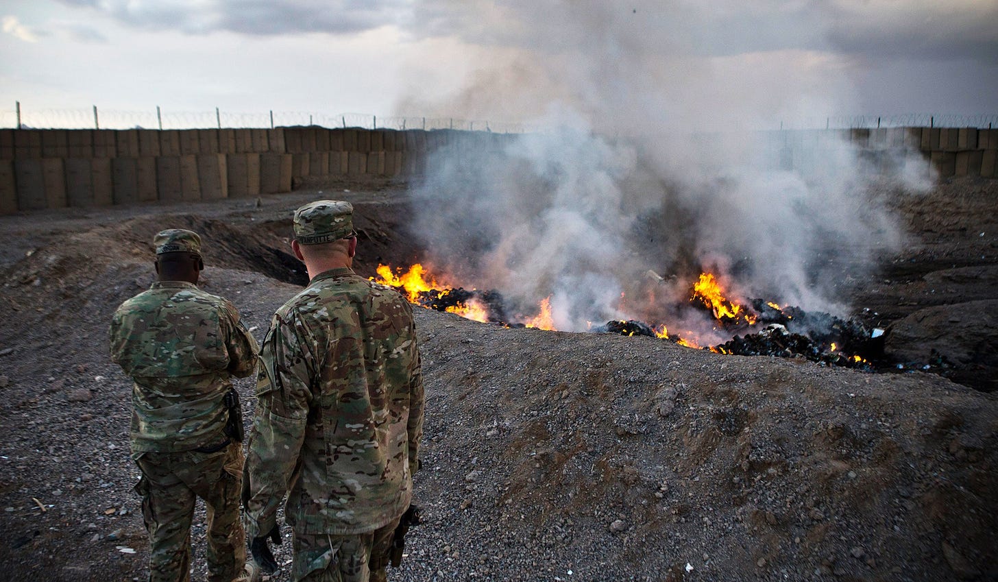 Two soldiers monitor a burn pit in Afghanistan.