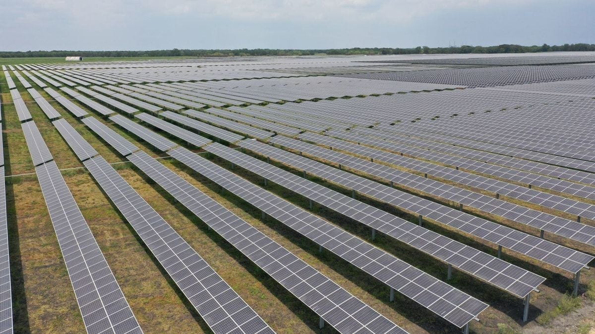 A field of solar panels on a grass plain. The solar panels stretch as far as the eye can see in long rows.