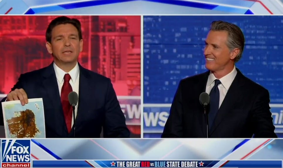 In a split-screen shot from the debate, Ron DeSantis holds up a map of feces reports in San Francisco while Gavin Newsom grins in disbelief