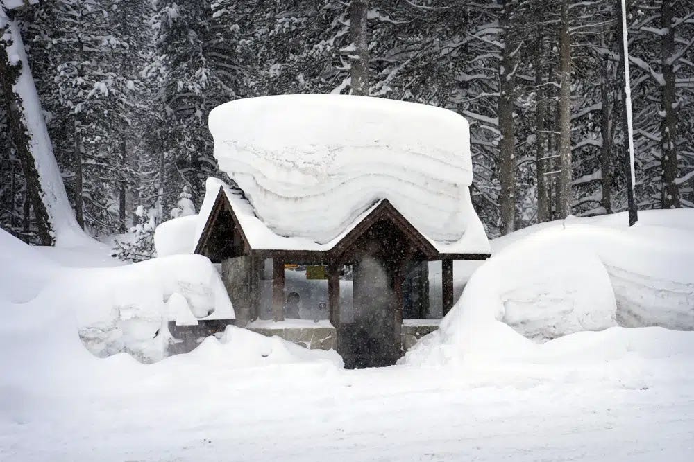 A person sits in a snow-covered bus stop Friday, Feb. 24, 2023, in Olympic Valley, Calif. California and other parts of the West are facing heavy snow and rain from the latest winter storm to pound the United States. (AP Photo/John Locher)