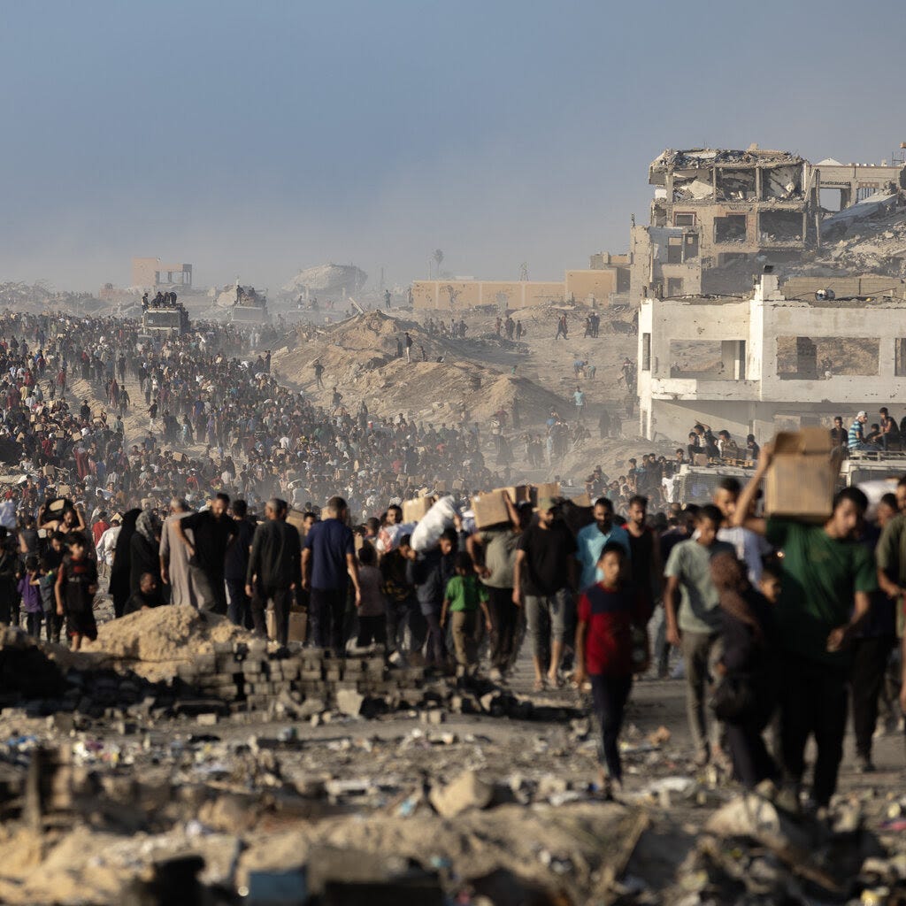 Crowds of Palestinians walking along a road covered with rubble. In the background are the remains of recently destroyed buildings.