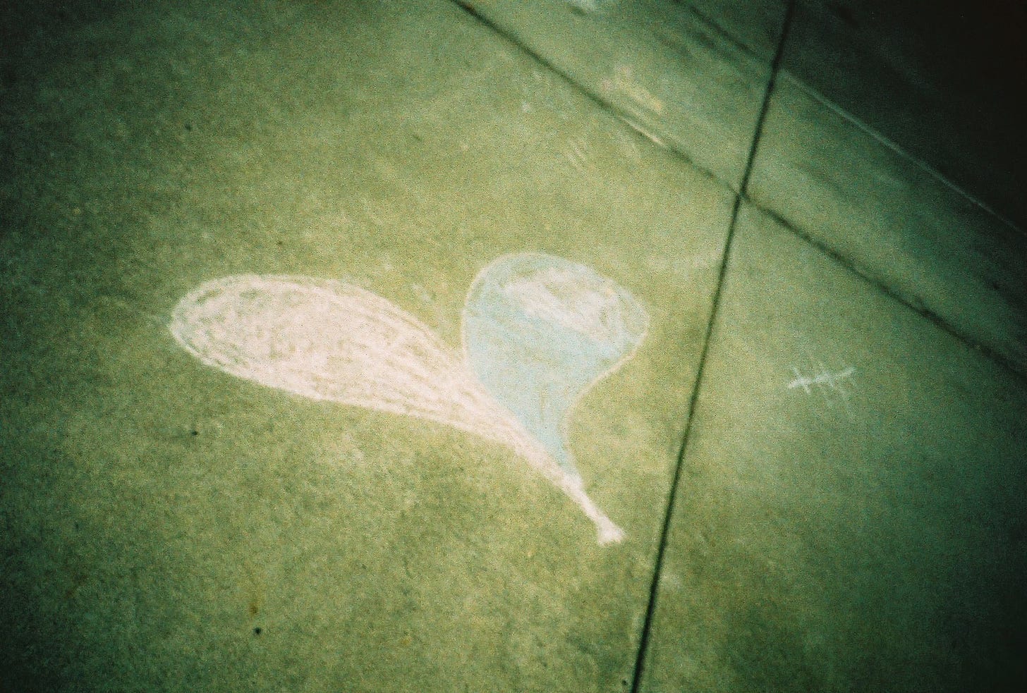 A photograph taken at a sharp angle shows a pink and blue heart drawn in sidewalk chalk on concrete.