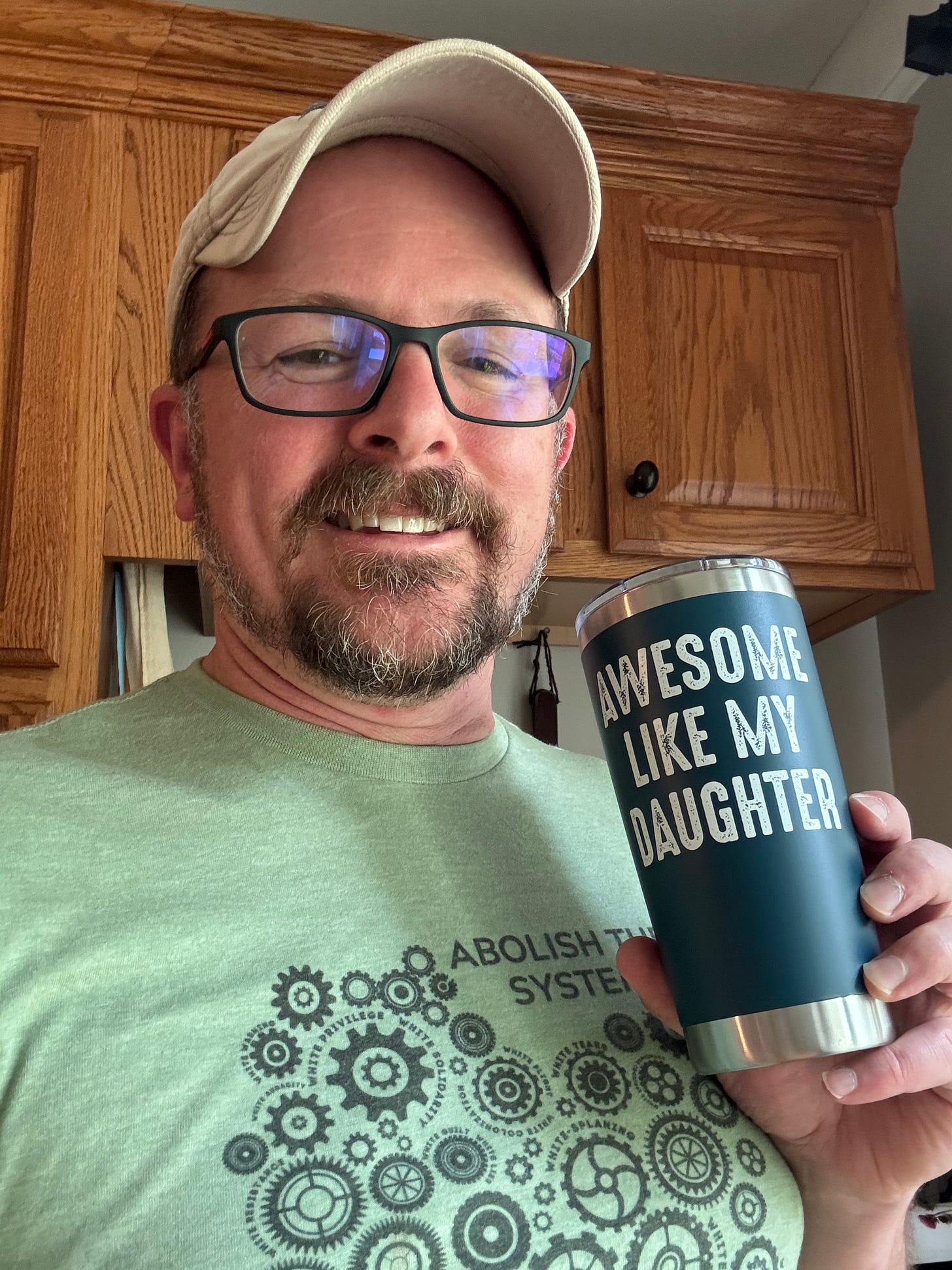 a dad holding a coffee mug labeled "Awesome Like My Daughter" in a shirt reading "Abolish the System"