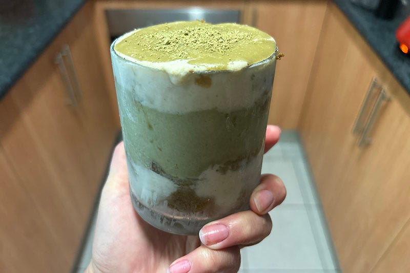 A hand holding a glass containing green matcha tiramisu.