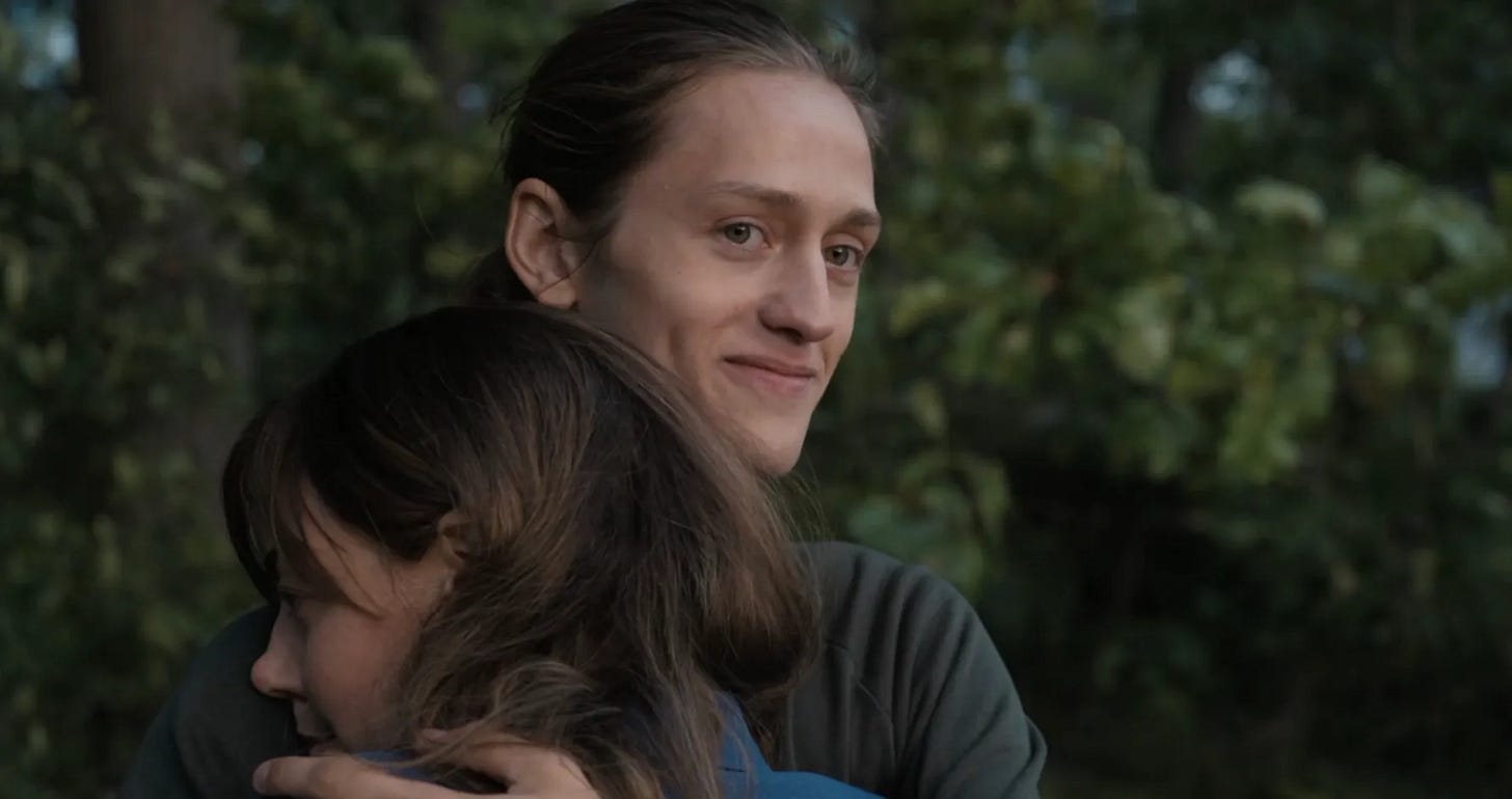 A young man holds a young woman. He smiles.