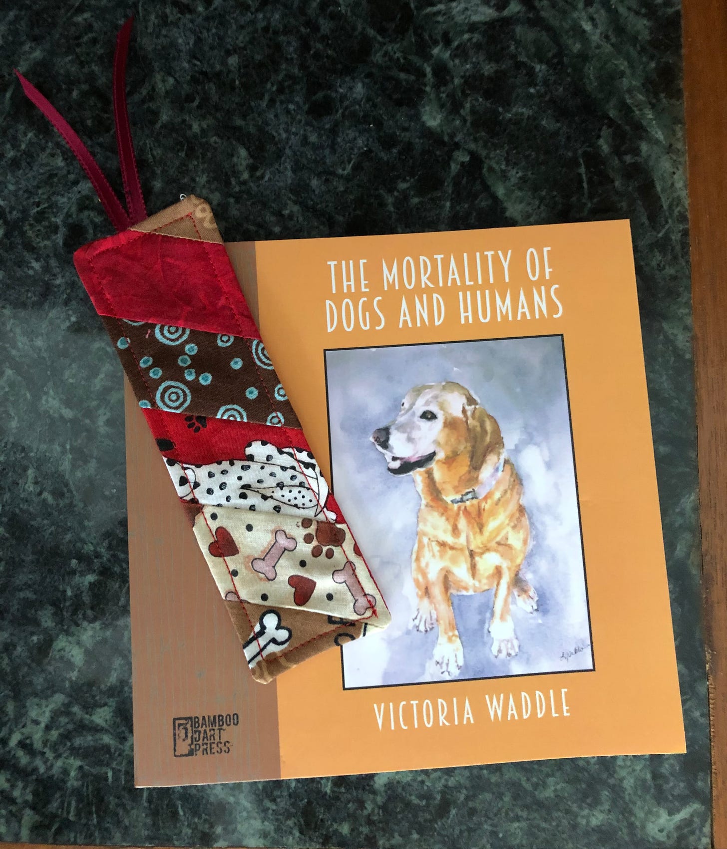 The chapbook ook The Mortality of Dogs and Humans, which has a watercolor painting of a Labrador retriever on teh cover, along with a fabric bookmark.