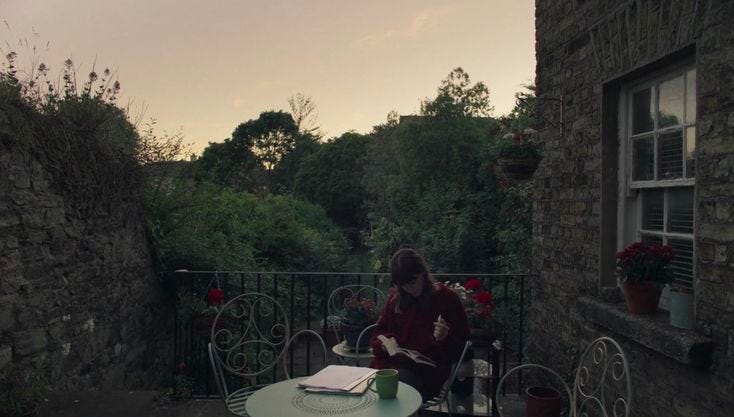 This may contain: a person sitting at a table with a book in front of them on a balcony