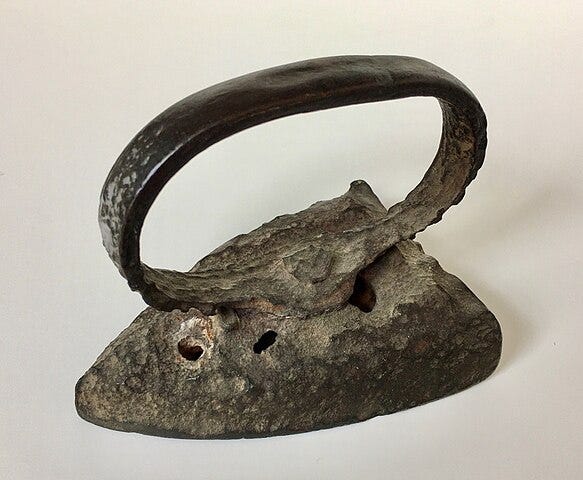 What looks like an iron for clothes, but also like a prehistoric relic: a pitted, heavy metal iron with an oval handle.
