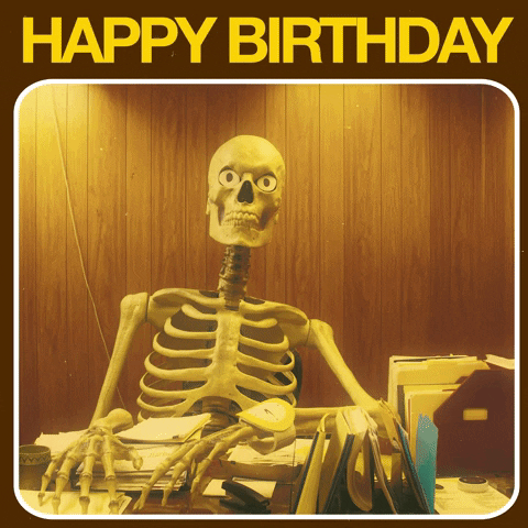 A skeleton sitting behind a desk with stacks of paper on it, balloons rising up behind them, and the text Happy Birthday at the top.