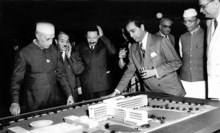 Homi Bhabha (glass in one hand and other on the table) showing Prime Minister Nehru the model of the Tata Institute of Fundamental Research (TIFR). 