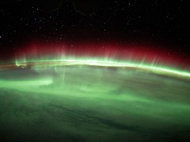 green and red aurora lights stream across earth horizon against black space