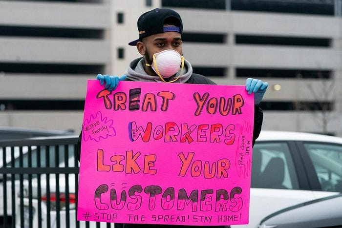 A man in a COVID mask holding up a protest sign saying: treat your workers like your customers