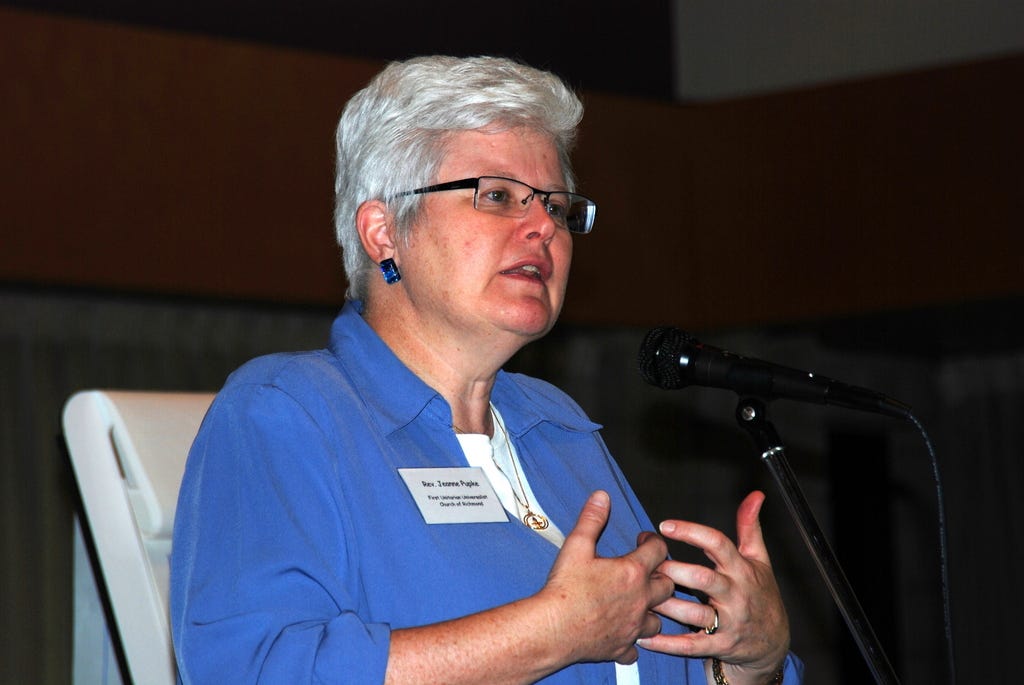 A woman with white hair and glasses dressed in a blue top