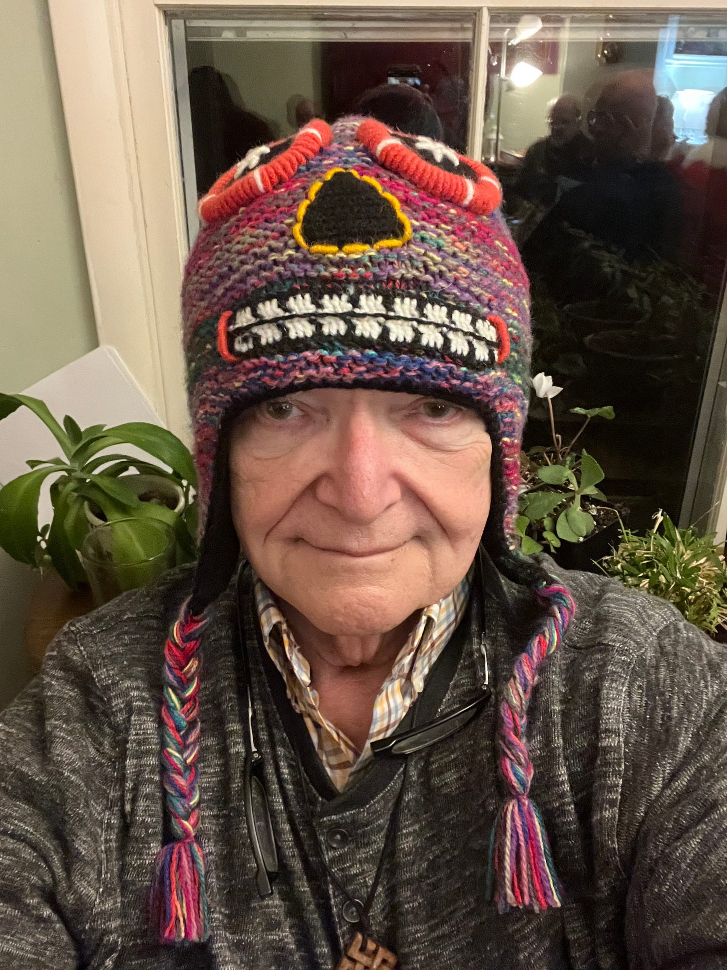 Photo of Mel Pine wearing a colorful knitted hat with large eyes, nose, and mouth.