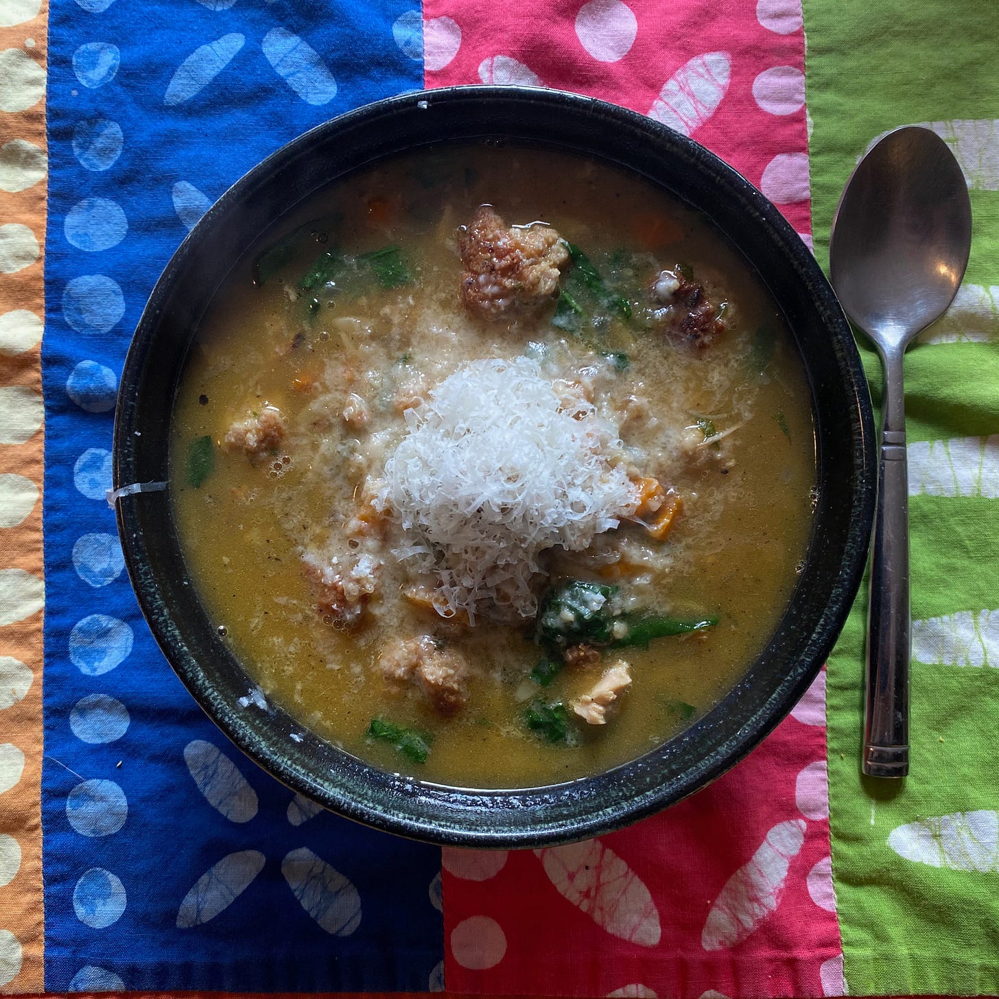 A ceramic bowl of soup, piled with grated Parmesan, on a colorful placemat.