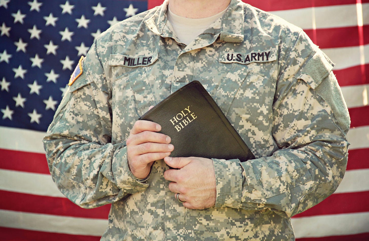 A us solder holds up a bible standing up in front of an American flag.