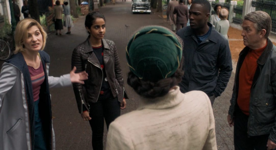 This image shows Team TARDIS (from left to right, Jodie Whittaker's Thirteenth Doctor, Mandip Gill's Yasmin "Yaz" Khan, Tosin Cole's Ryan Sinclair, and Bradley Walsh's Graham O'Brien) arrayed around Rosa Parks (played by Vinette Robinson), whose back is to camera. All five characters stand on a street in 1955 Montgomery, Alabama. This image shows Team TARDIS (from left to right, Jodie Whittaker's Thirteenth Doctor, Mandip Gill's Yasmin "Yaz" Khan, Tosin Cole's Ryan Sinclair, and Bradley Walsh's Graham O'Brien) arrayed around Rosa Parks (played by Vinette Robinson), whose back is to camera. All five characters stand on a street in 1955 Montgomery, Alabama.