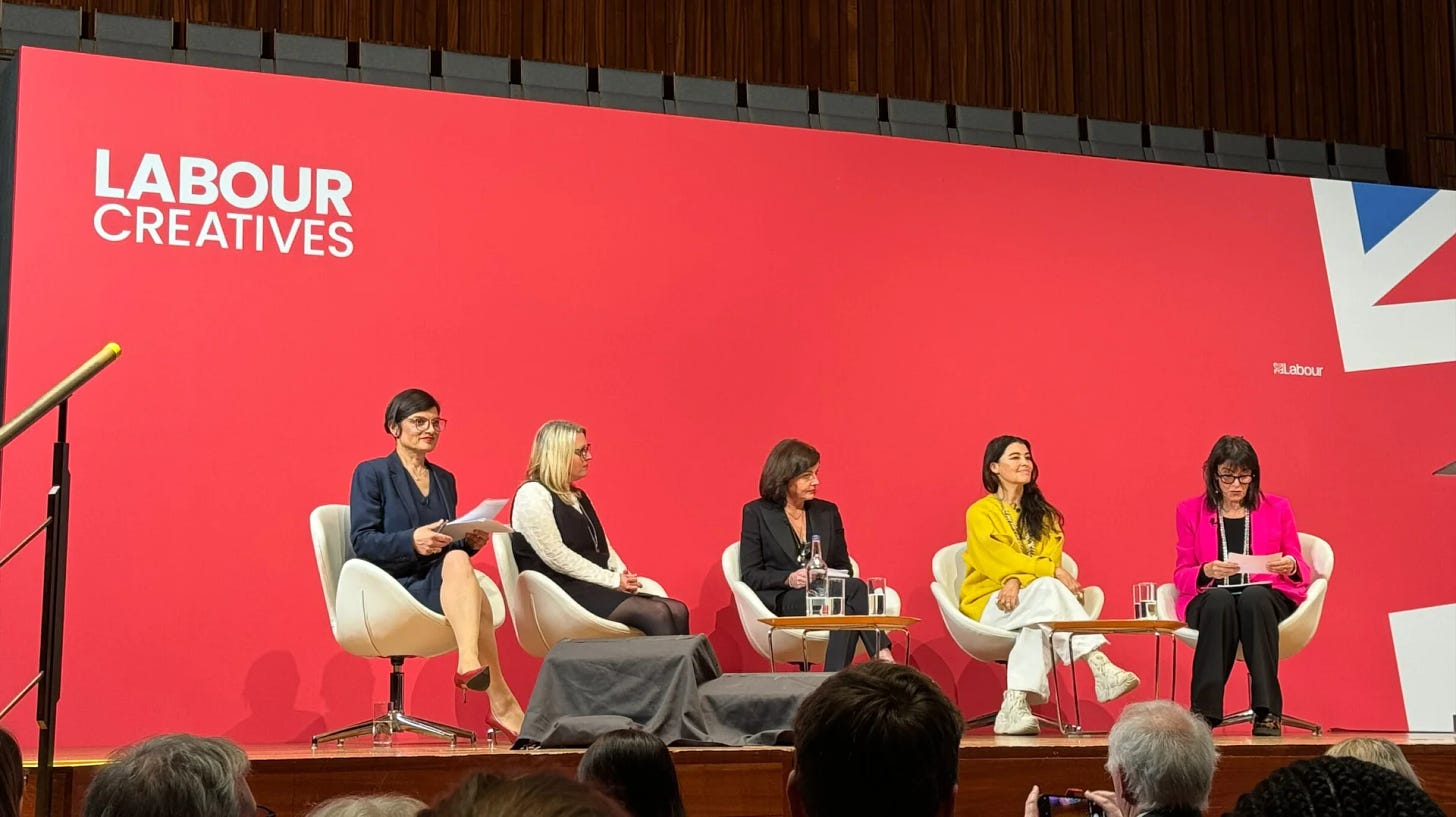 A photograph of 5 people sitting on a stage, in front of a red background, that reads LABOUR CREATIVES