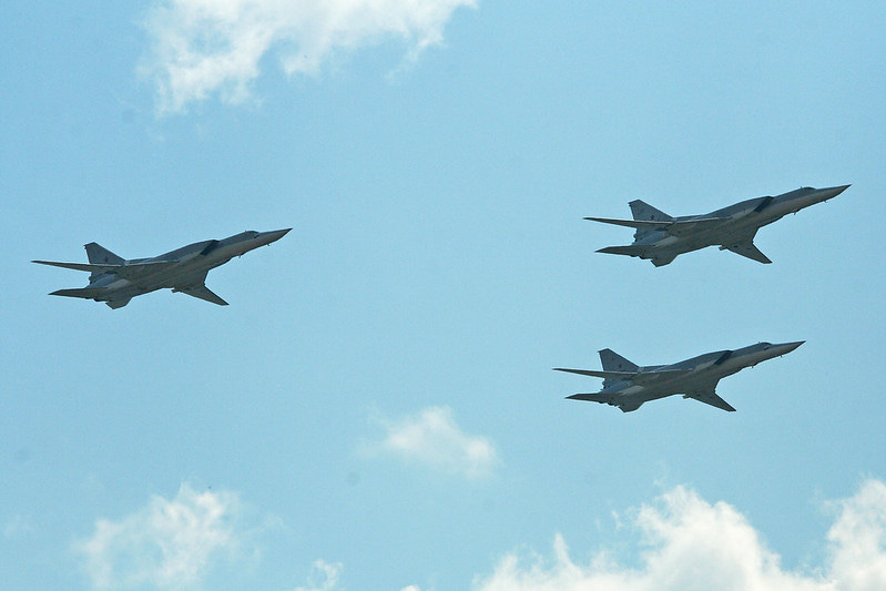 Three Tu-22M3 Backfires fly in formation, against a blue sky.