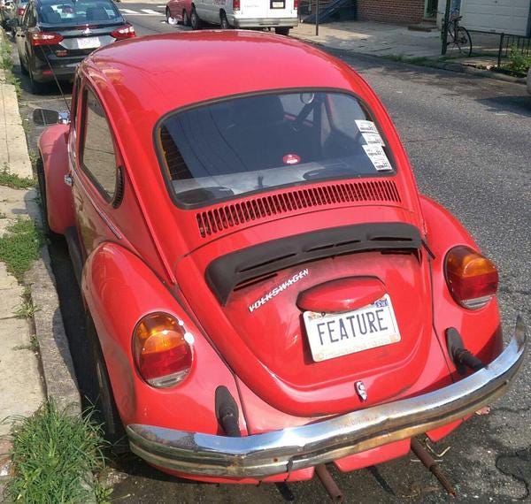 A red Volkswagen Beetle, also known as a Bug, with a license plate that says Feature