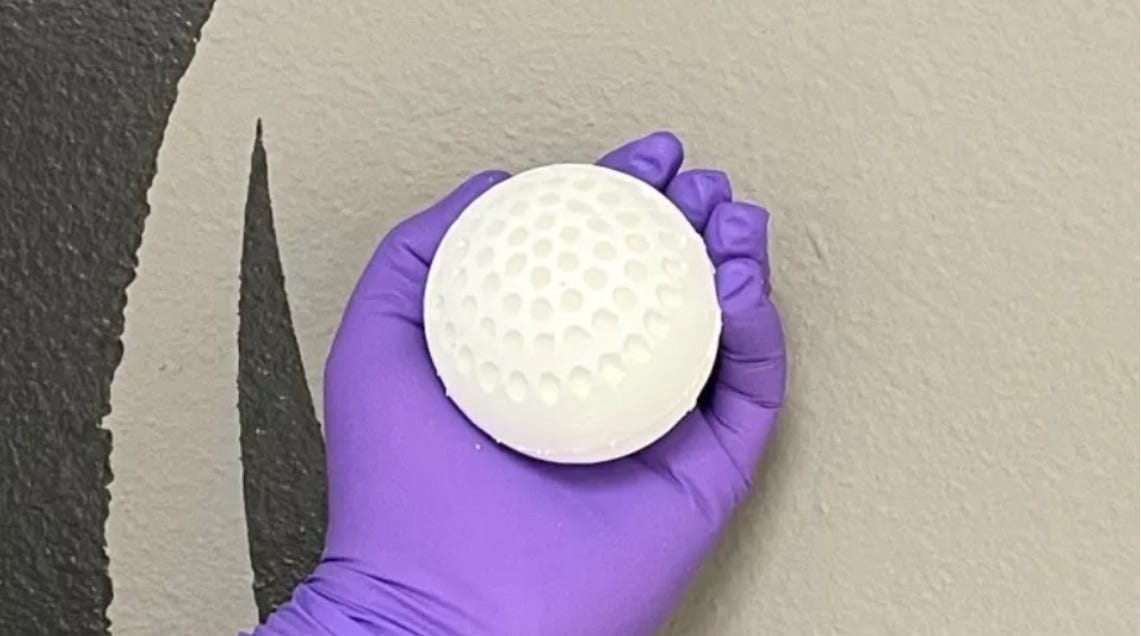 A photo of a gloved hand holding a white, pockmarked ball of Spiritus' carbon-absorbing sorbent.