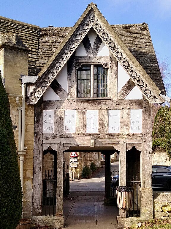 A wooden lychgate with an Elizabethan style. A mullioned window is in the upstairs section. A wooden lychgate with an Elizabethan style. A mullioned window is in the upstairs section.