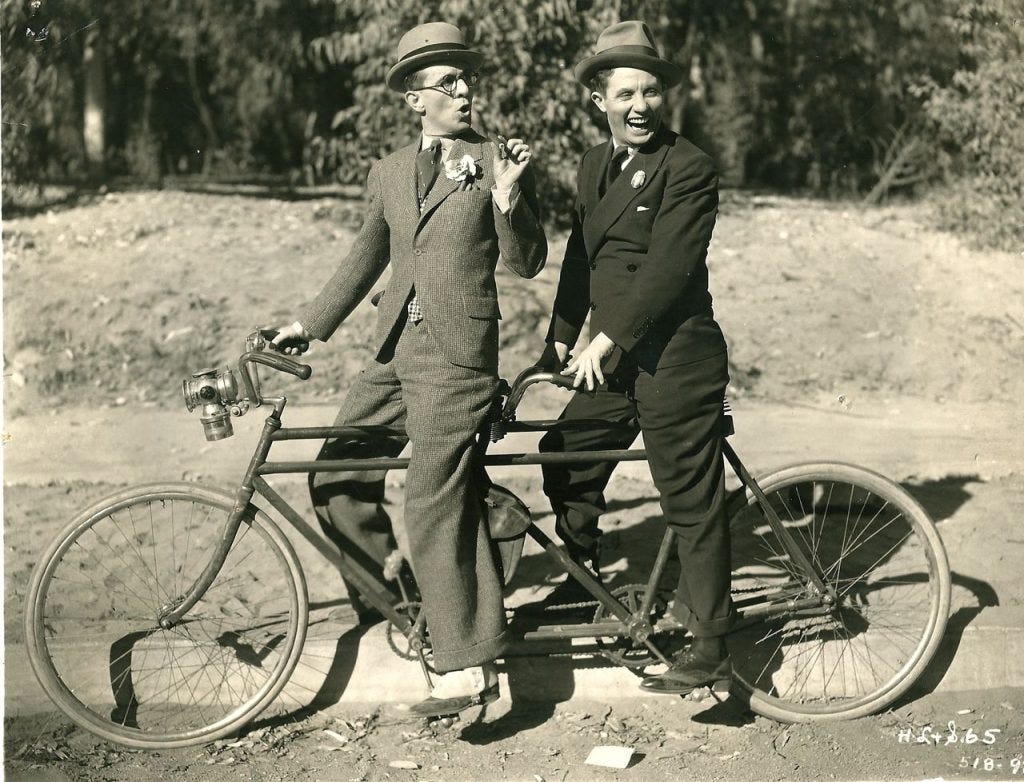 Bert Wheeler and Robert Woolsey ride a bike.