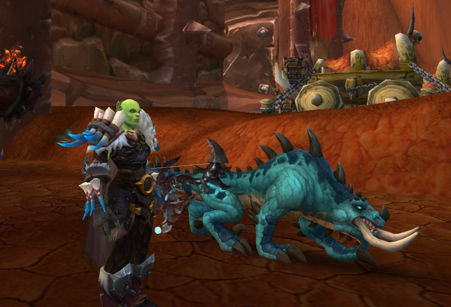 Screencap from World of Warcraft showing an bald female orc hunter with a large blue-green lizard beast outside the gates of a grim desert city.