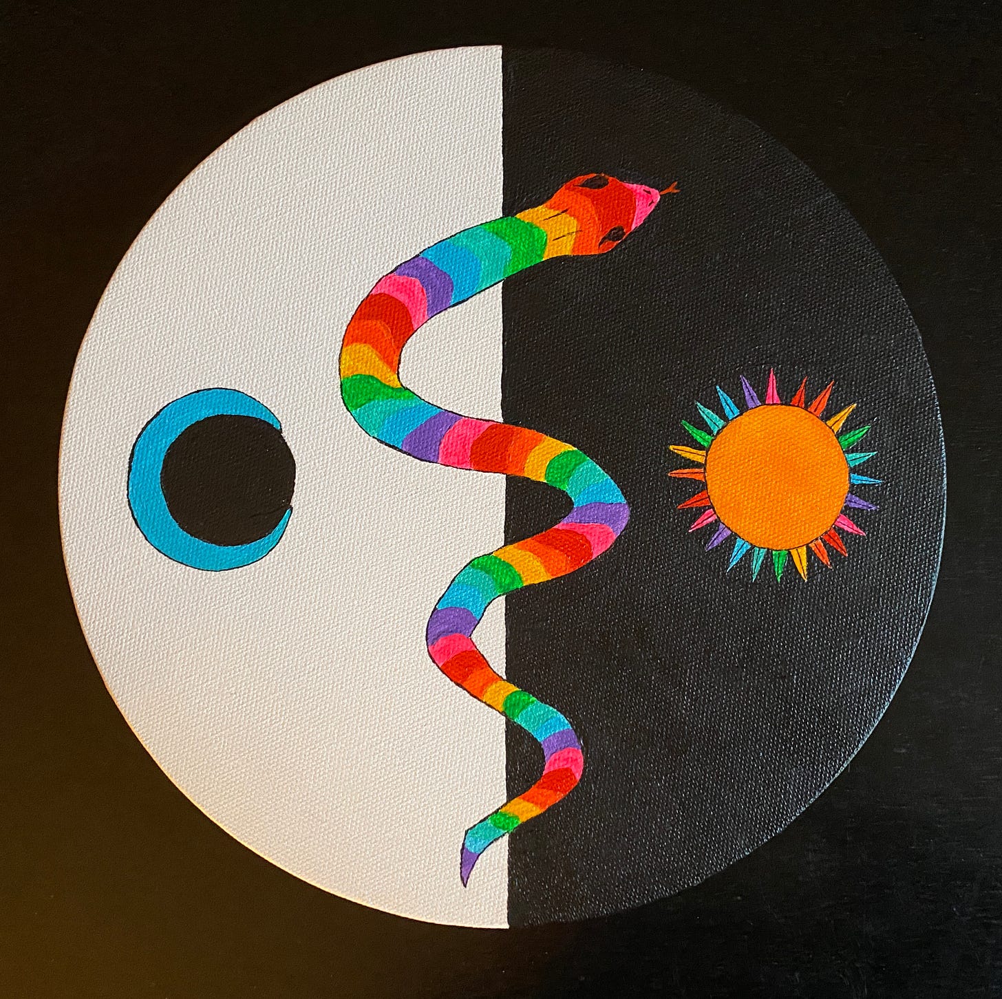 A round canvas painted with a rainbow snake against a black and white background, with the sun on the dark side and the moon on the light side