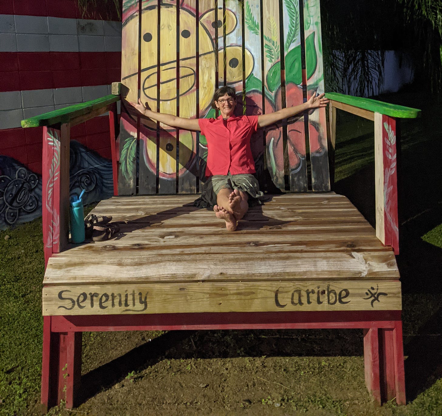 picture of me sitting in an enormous wooden beach chair, with my arms spread from side to side, still not wide enough for me to reach the armrests, and my legs straight out in front of me, nowhere near the end of the seat.
