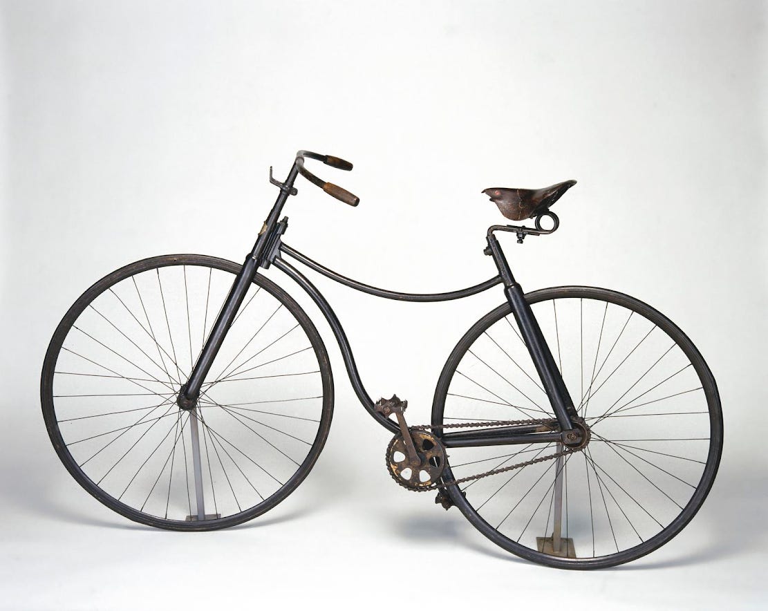 A Victorian bicycle with a metal frame, pictured from the side again a white background.