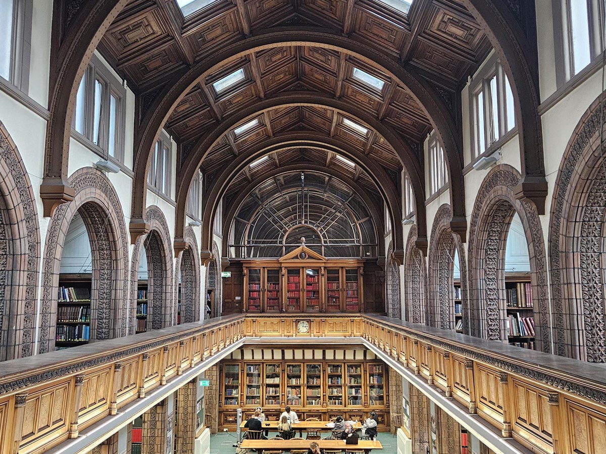 View from the balcony of a library reading room - arched alcoves around the balcony and people sitting at desks below