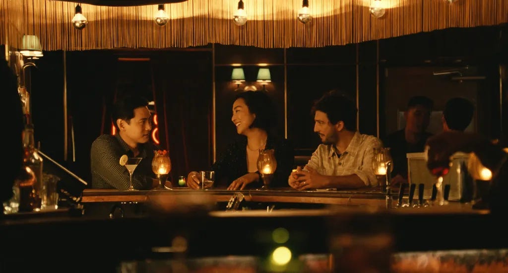 Cena do filme Vidas Passadas, com o trio central num balcão de bar